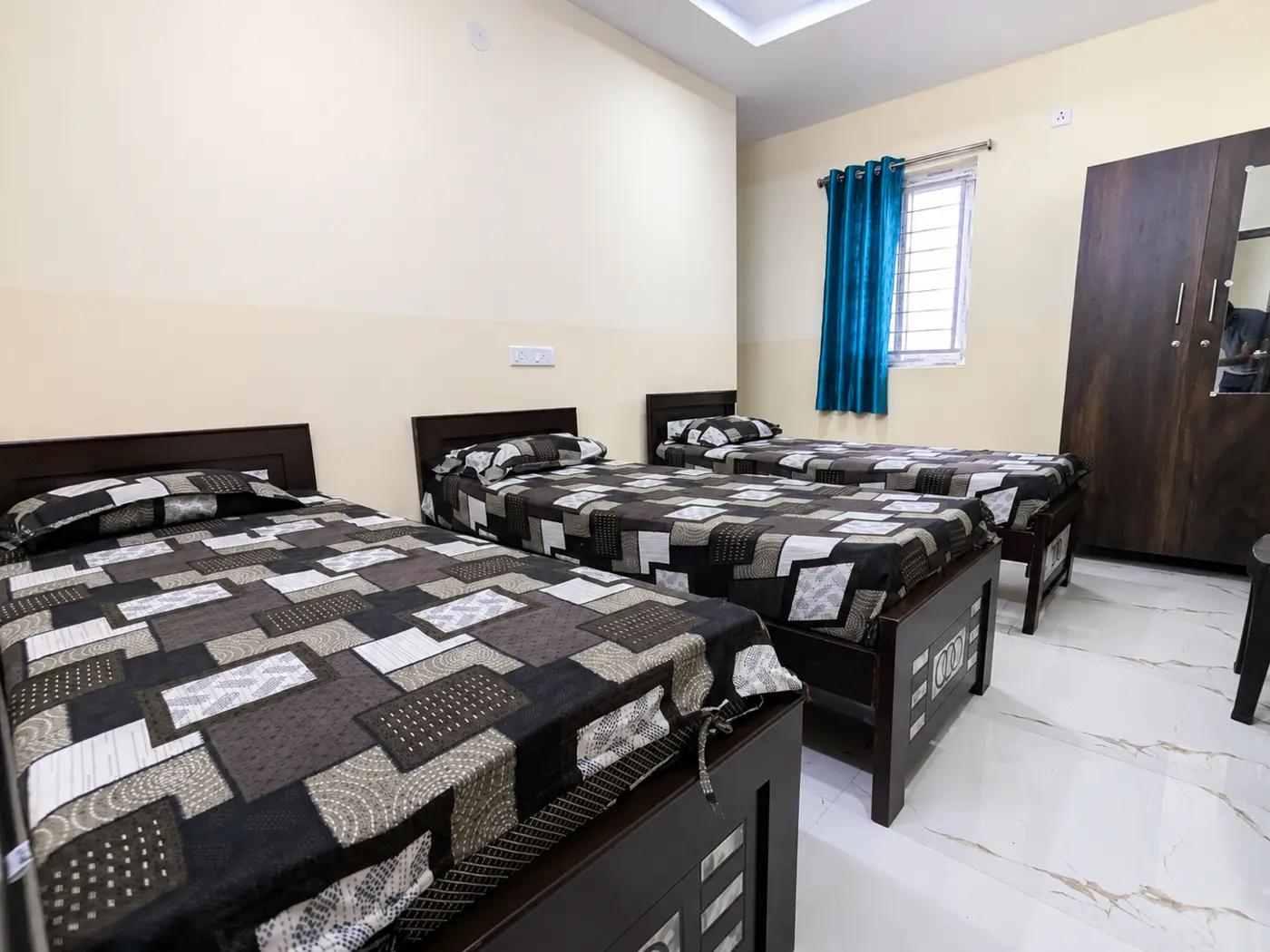 Three single beds arranged along the walls of a sharing room with a wardrobe