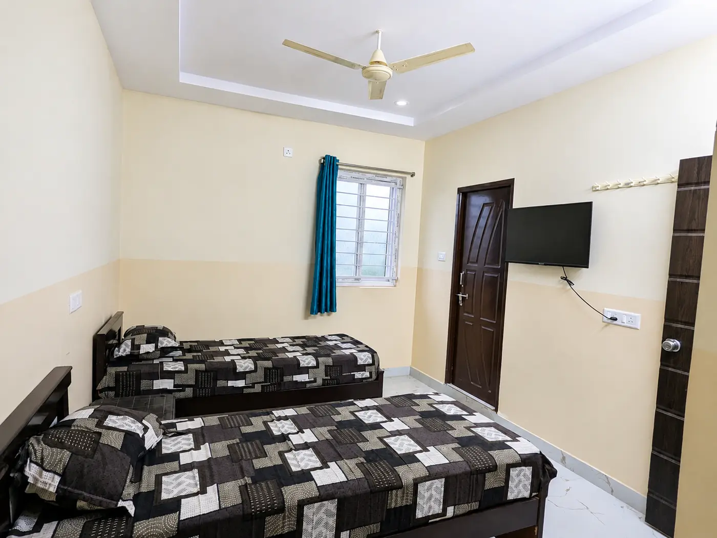 A room with single beds, a ceiling fan and a wall-mounted television