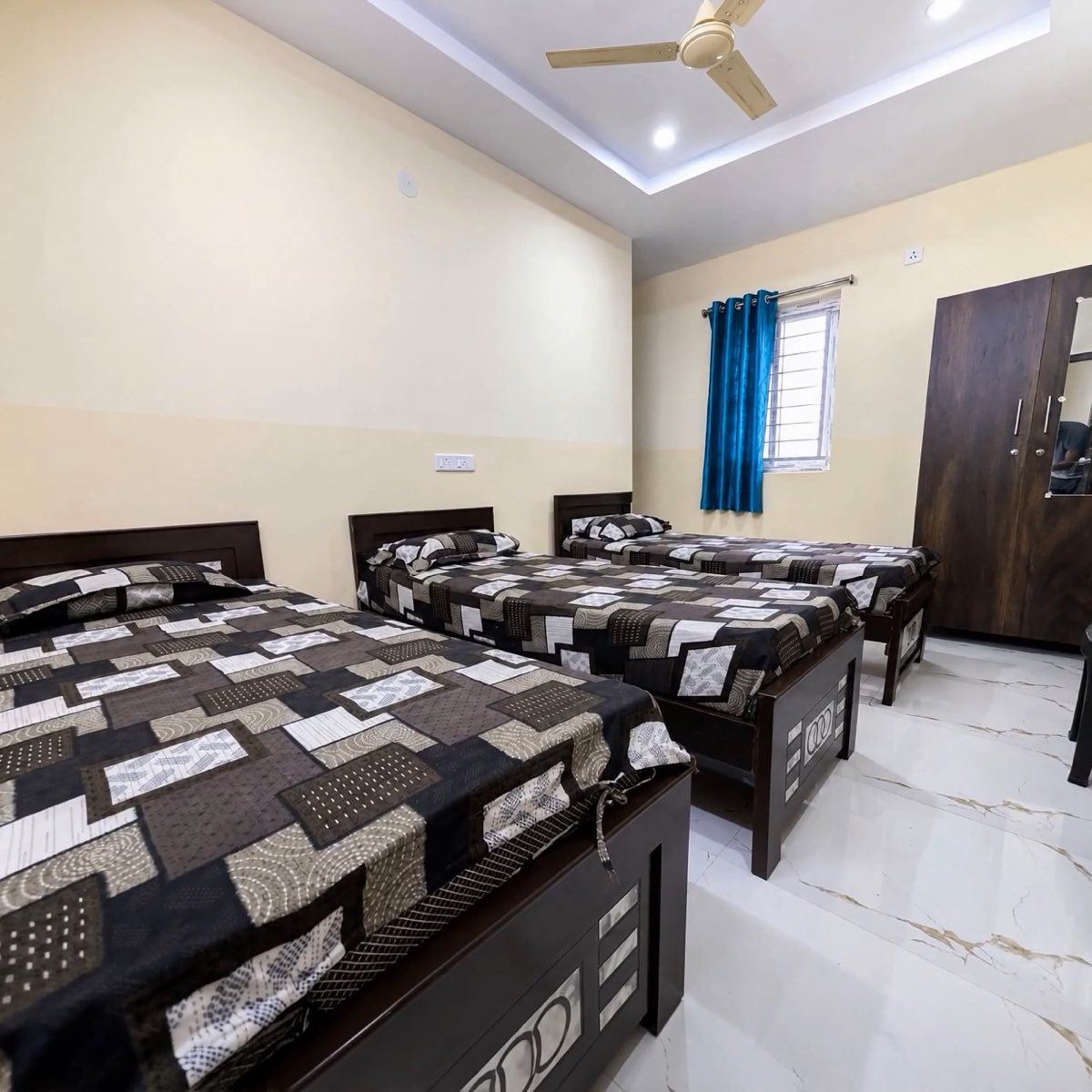 Four single beds with a ceiling fan, wardrobe and curtained window in a four-sharing room